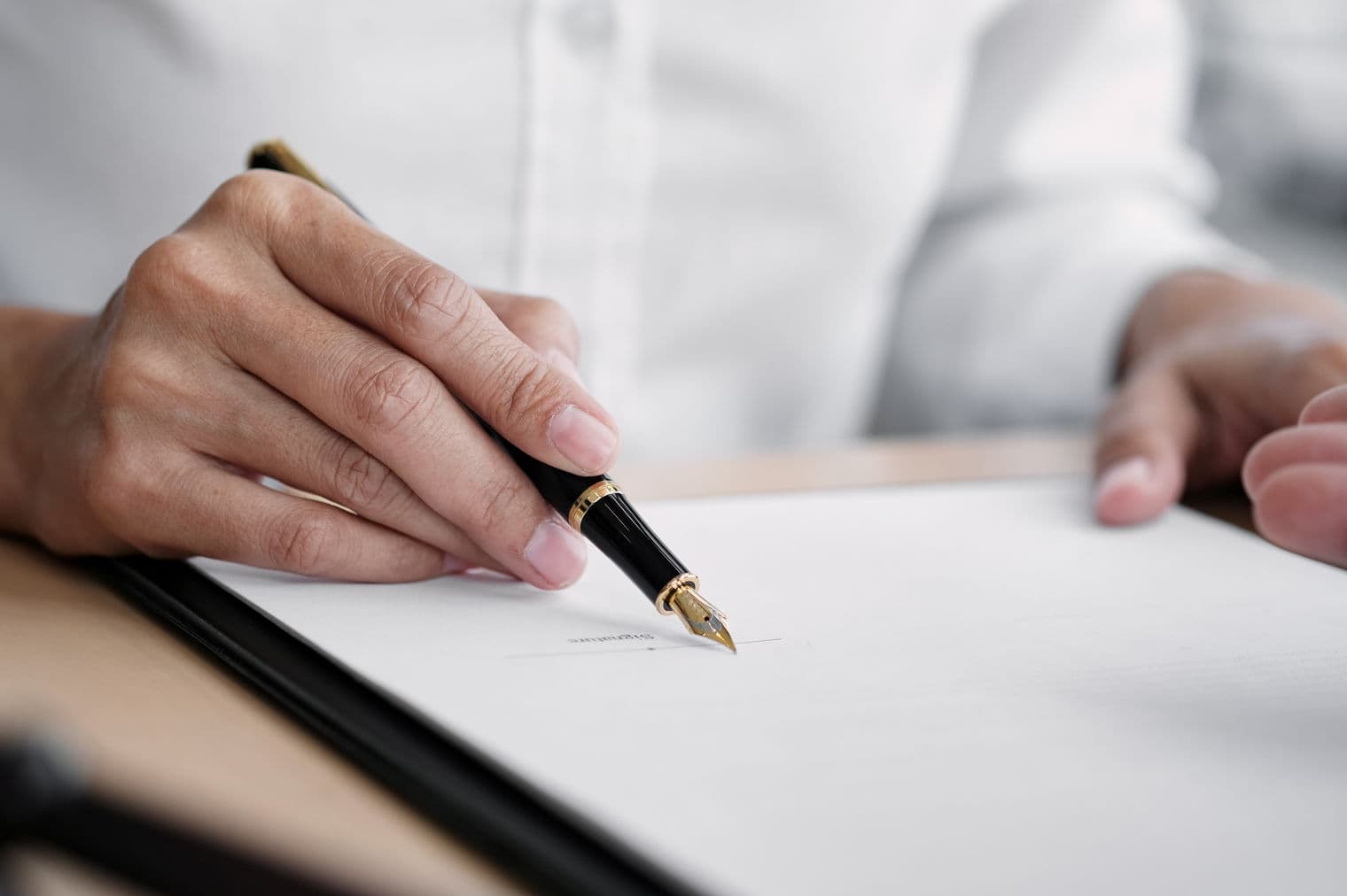 A person signs a document with a black and gold fountain pen.