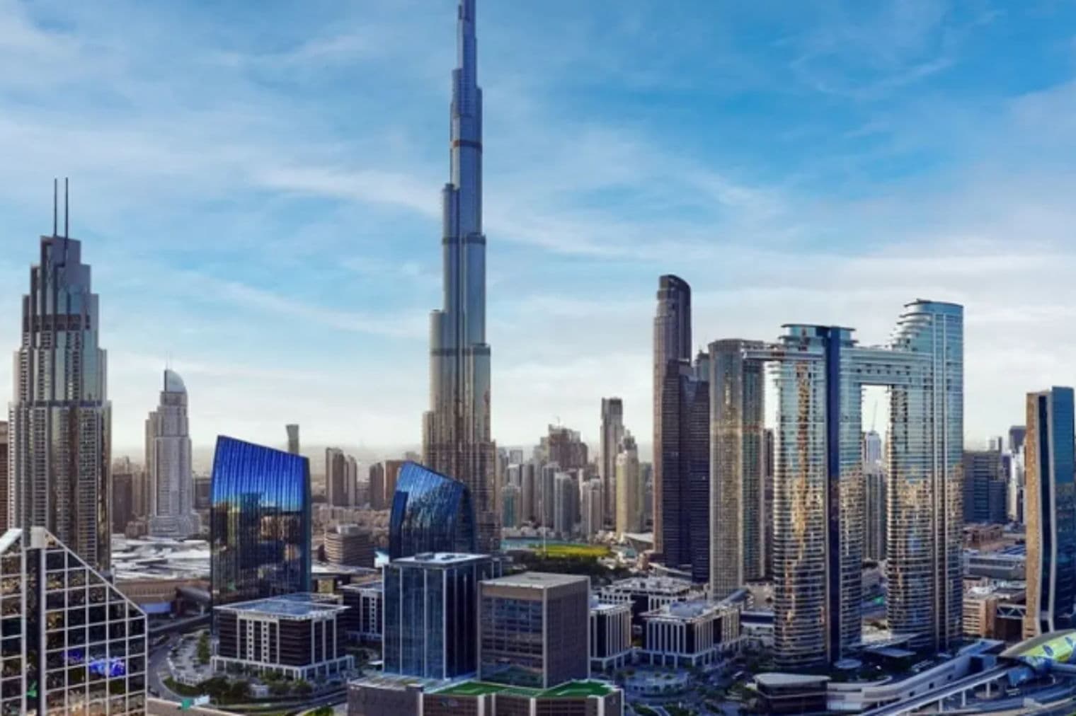 Dubai skyline with Burj Khalifa towering over modern buildings under a blue sky. Roads and highways wind through the cityscape.