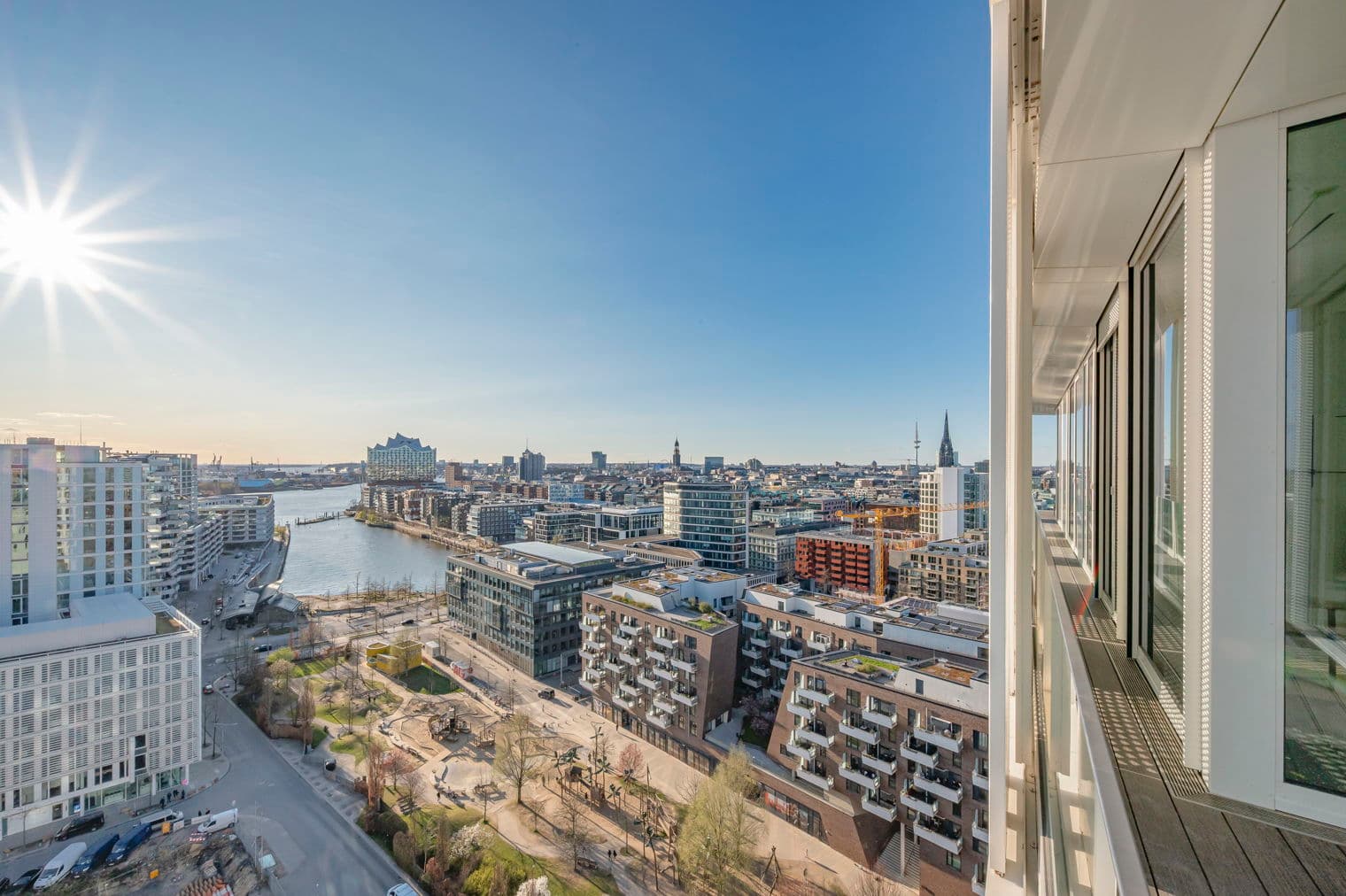 Blick von einem Hochhausbalkon mit Blick auf Hamburg, Deutschland. Moderne Gebäude, ein Fluss und ein klarer, blauer Himmel sind sichtbar.