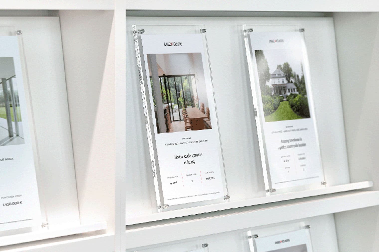 Real estate listings in clear acrylic frames on a white shelf. The listings feature property photos and descriptions.