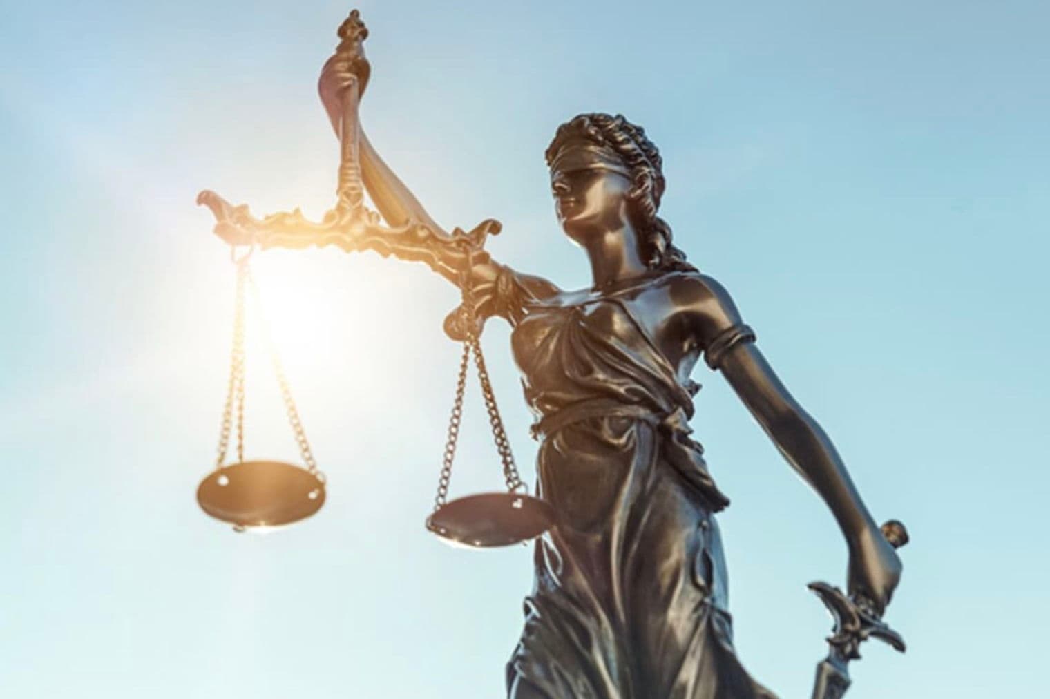 Statue en bronze de Dame Justice avec des balances et une épée sur fond de ciel bleu.