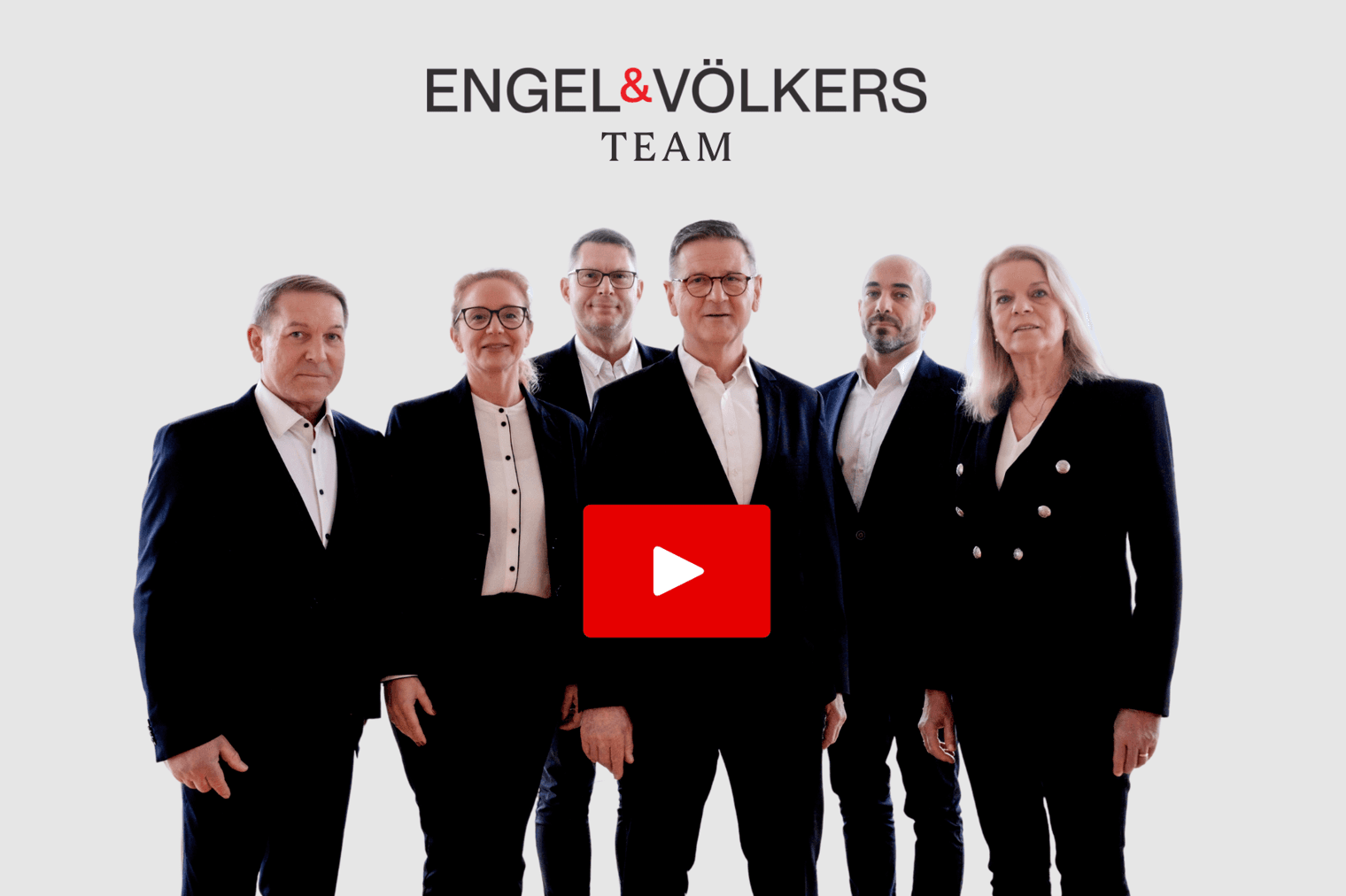 Engel & Völkers Teamfoto. Sechs Fachleute in schwarzen Anzügen stehen vor einem weißen Hintergrund. Eine rote Wiedergabetaste ist überlagert.