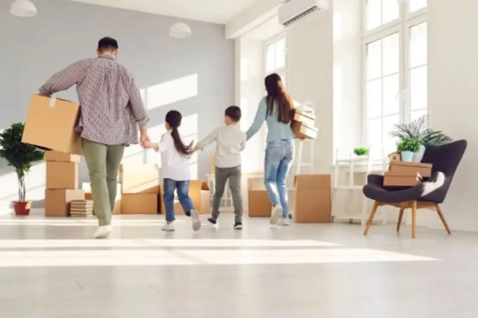 A family of four moves into a bright, white room filled with cardboard boxes. The parents hold hands with their children as they walk into their new home.