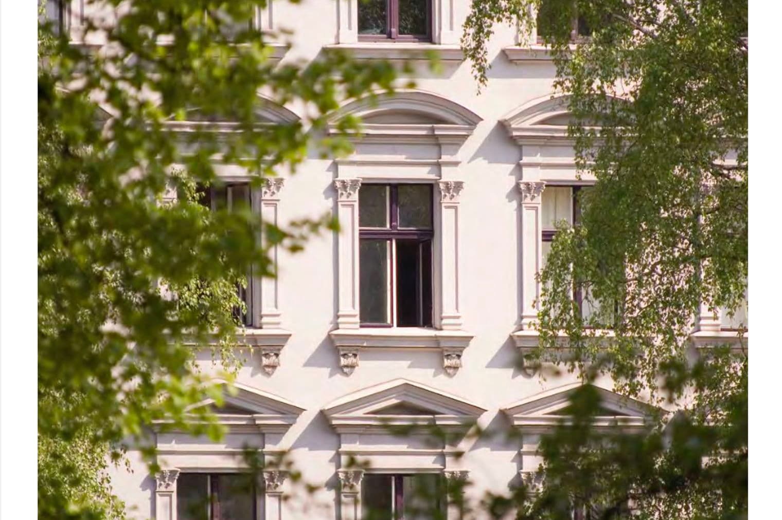 Facade of a white building with dark windows, framed by green trees. Engel & Völkers Commercial logo at the top.