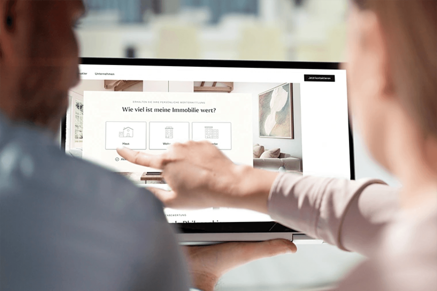 Ein Paar schaut auf den Bildschirm eines Laptops mit einer Immobilien-Website, eine Hand zeigt auf die Option "Haus".