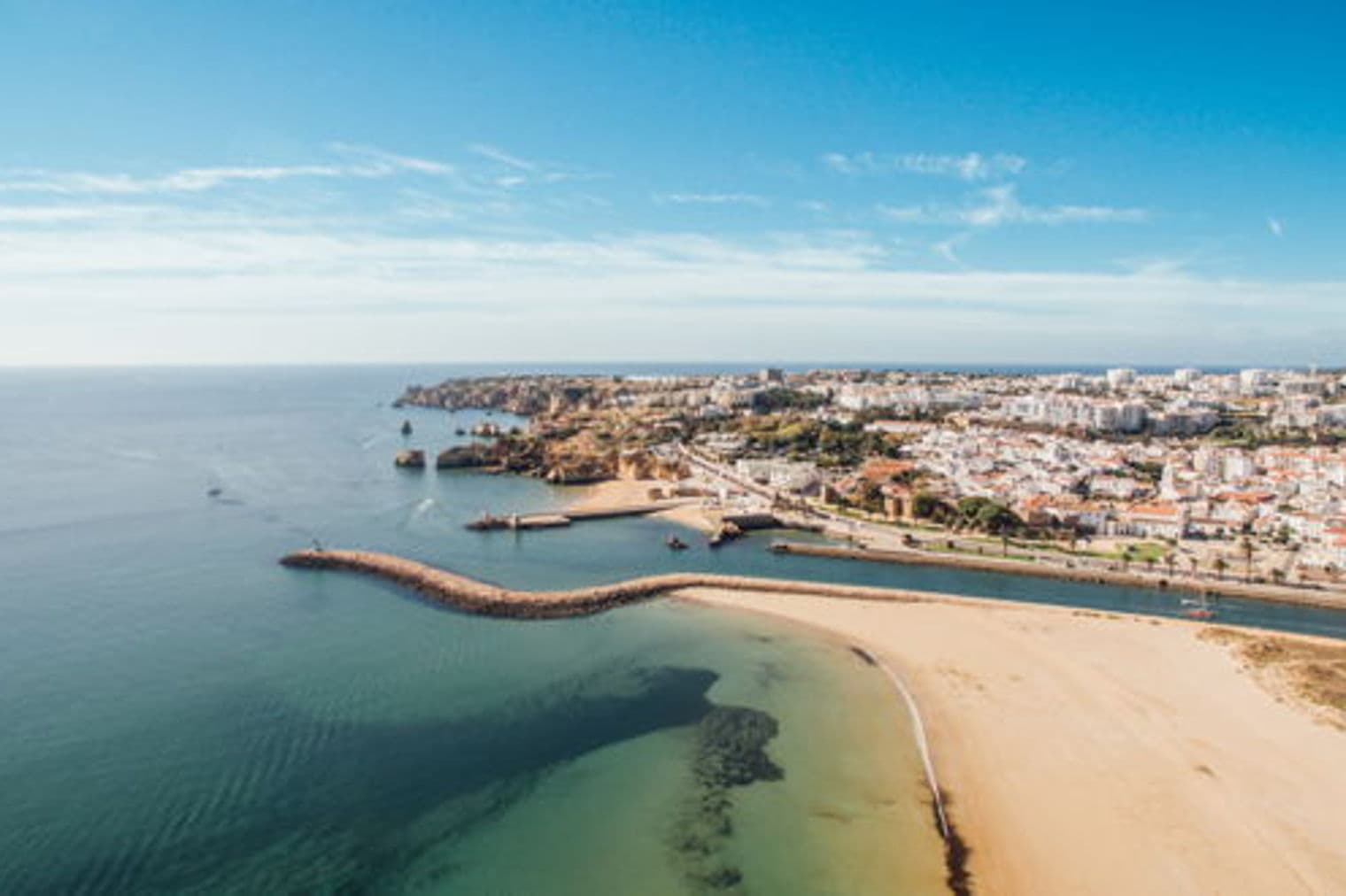 Aerial view of Lagos, Portugal, featuring a sandy beach, turquoise water, and a city with white buildings under a blue sky.