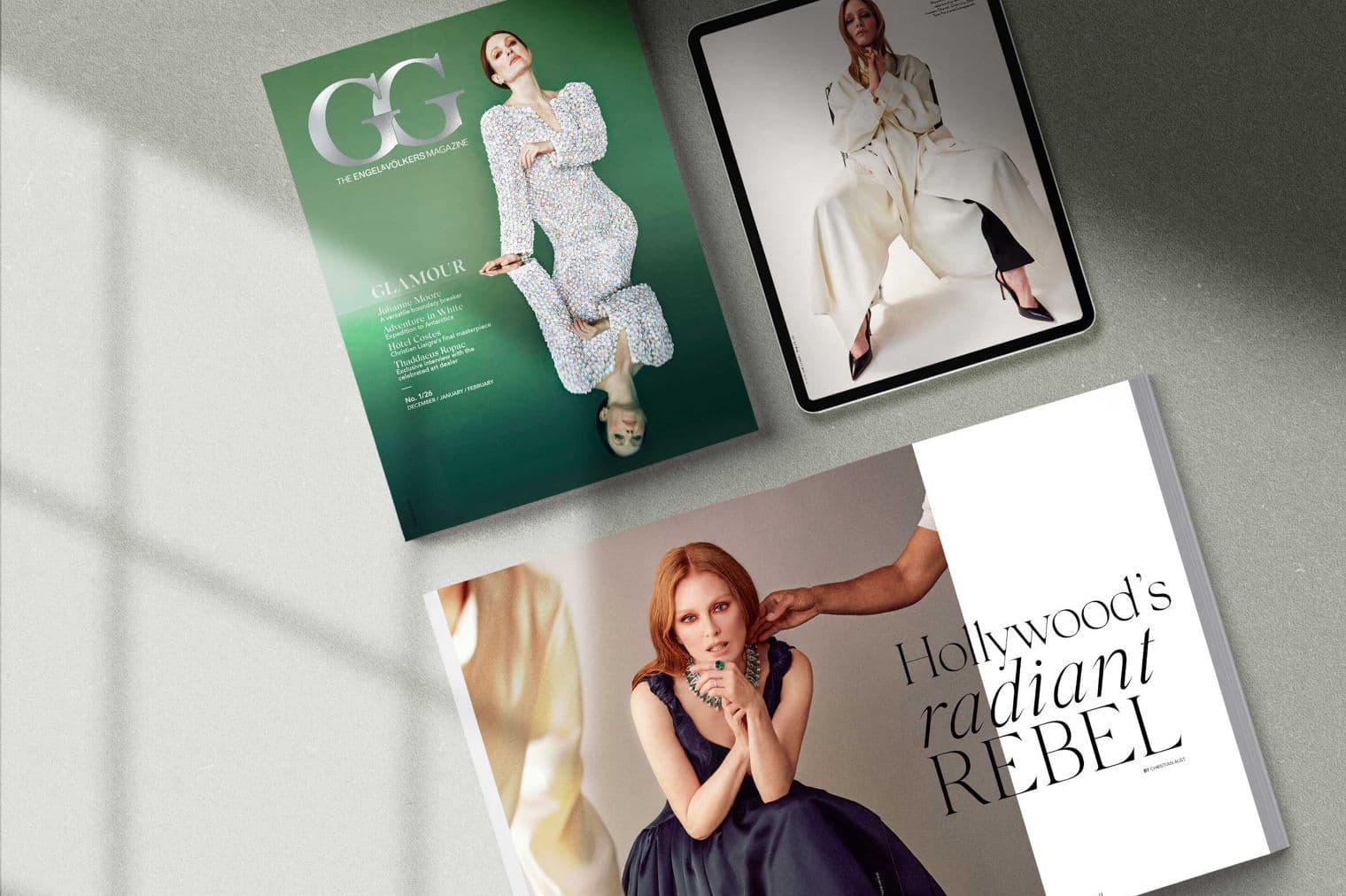 Three Engel & Volkers magazines and a tablet are on a gray surface. The magazine covers feature Julianne Moore.
