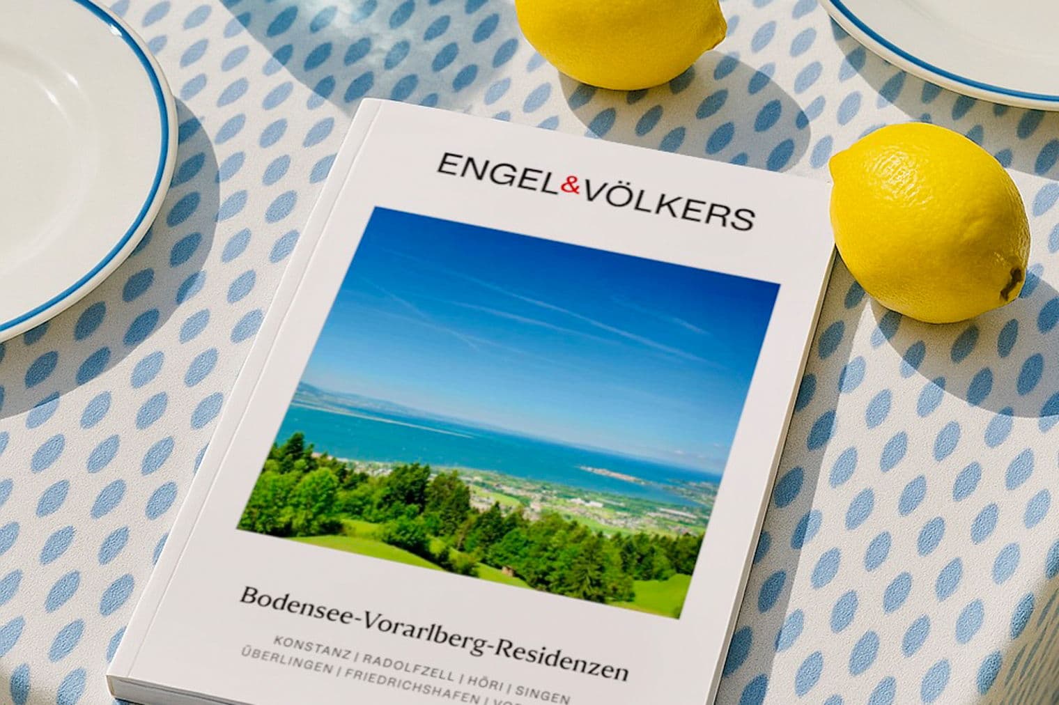 Engel & Völkers catalog on a blue patterned tablecloth with lemons, glasses, and plates.