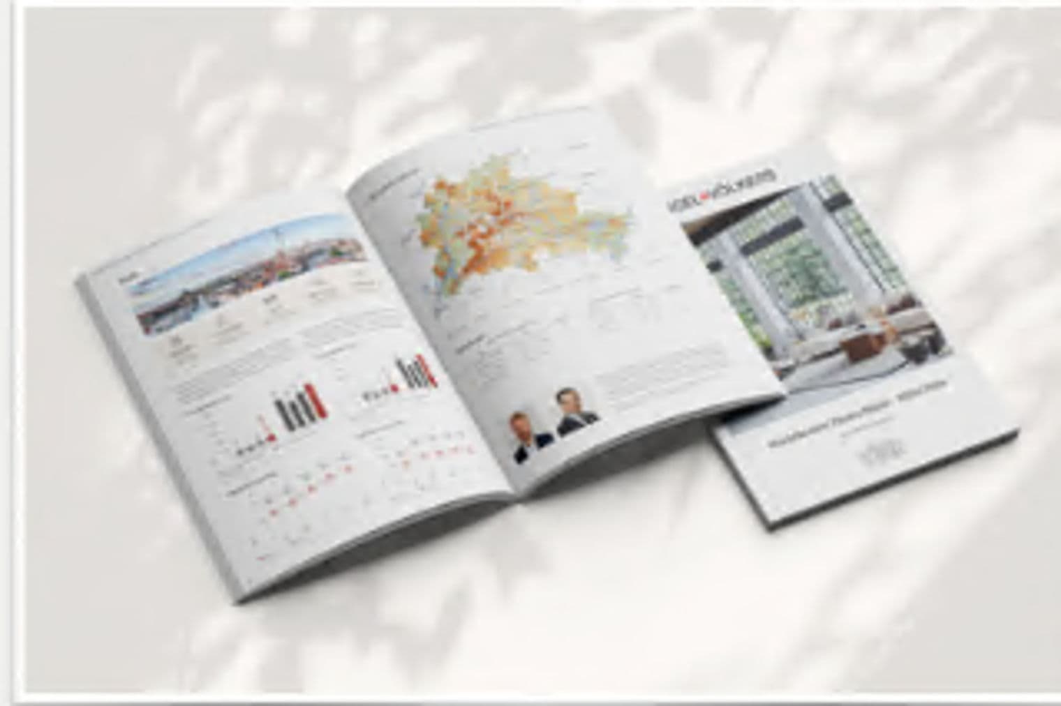 Immobilienbroschüre geöffnet, die Immobiliendaten, Karten und Innenfotos anzeigt. Weißes Cover mit schwarzem Text. Sonnenlicht und Schatten.