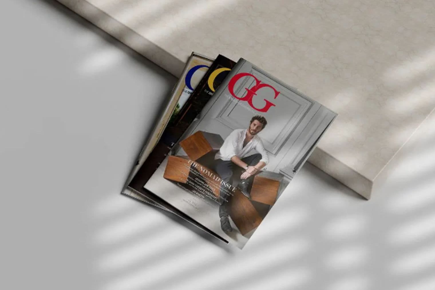 Drei Zeitschriften liegen mit Schatten auf einer weißen Oberfläche gestapelt. Auf der obersten Zeitschrift sind ein Mann und die Buchstaben „GG“ in Rot abgebildet.