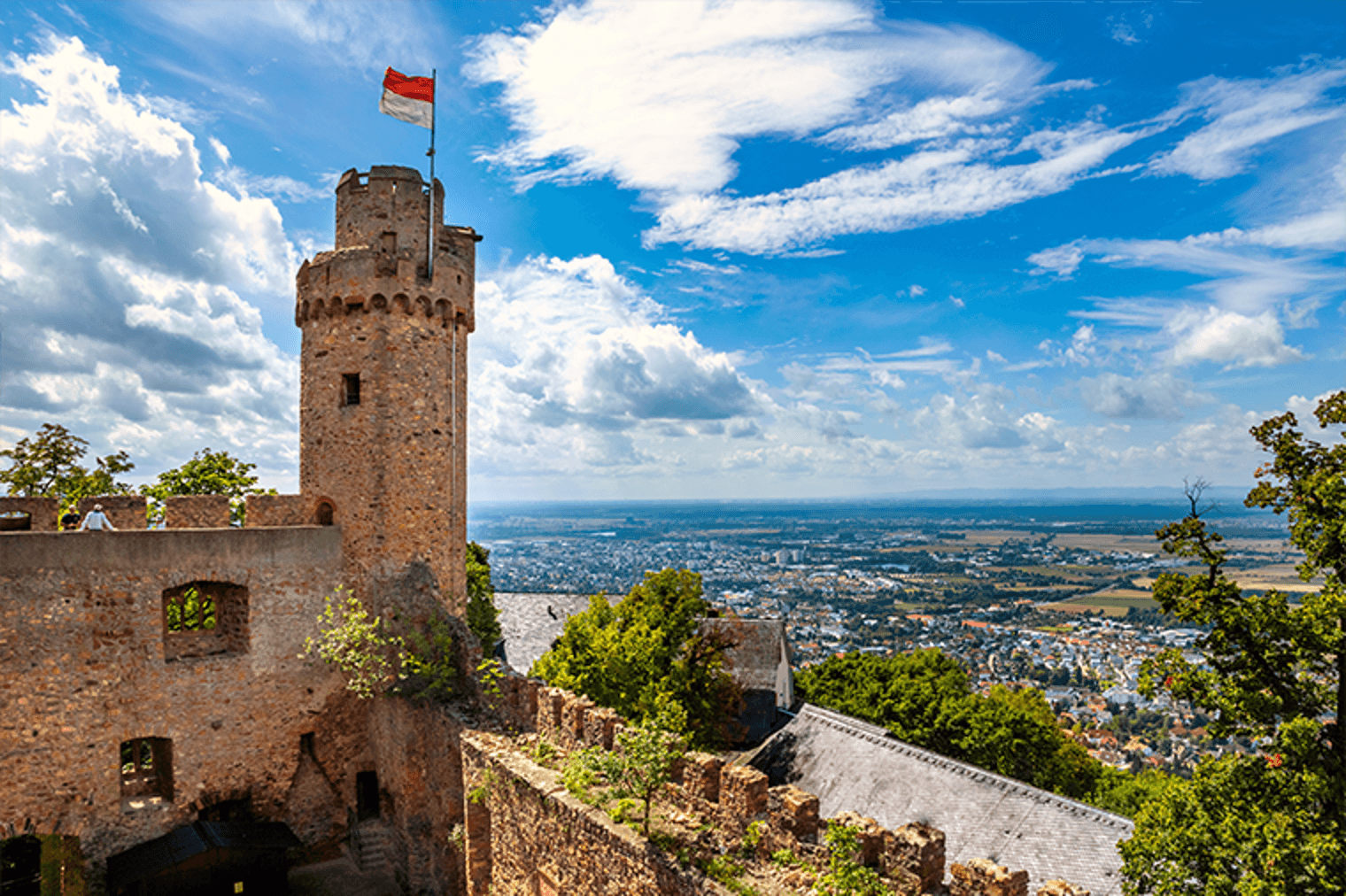 Blick von der Festung Königstein, Deutschland, auf einen Steinturm mit einer rot-weißen Flagge und eine Stadt in der Ferne.