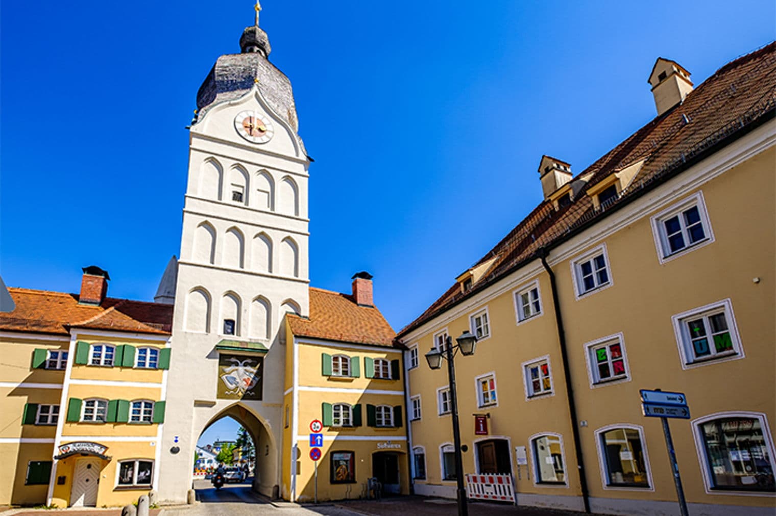 Stadttor mit einem hohen Glockenturm und gelben Gebäuden unter einem klaren blauen Himmel.