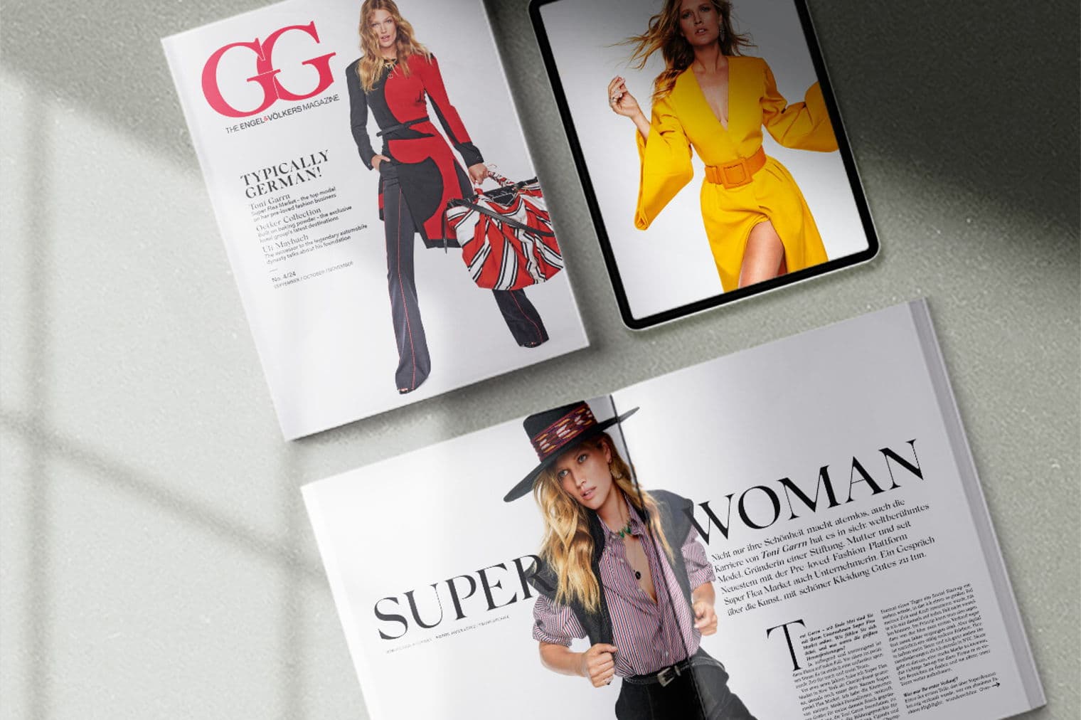 Close-up of three magazines and a tablet. The magazines feature models on the covers. The tablet displays a model in a yellow dress.