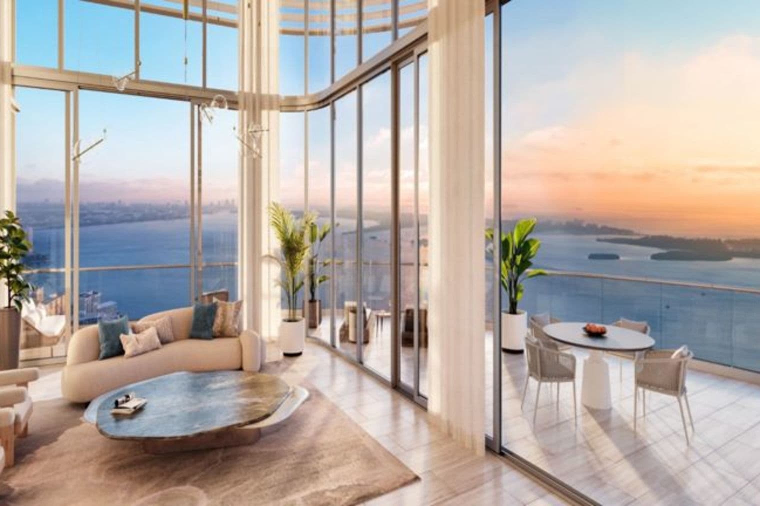 A modern condo living room with floor-to-ceiling windows overlooking a bay at sunset. Beige sofa, unique coffee table, and balcony with table and chairs.