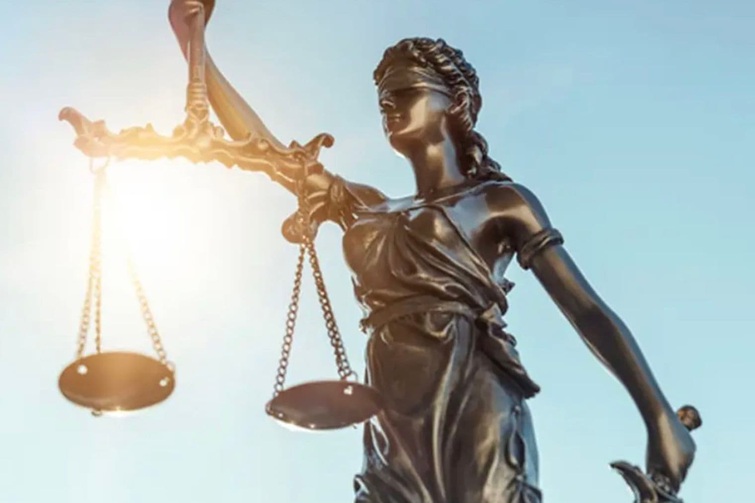 Bronzestatue der Justitia mit Waage und Schwert vor blauem Himmel.