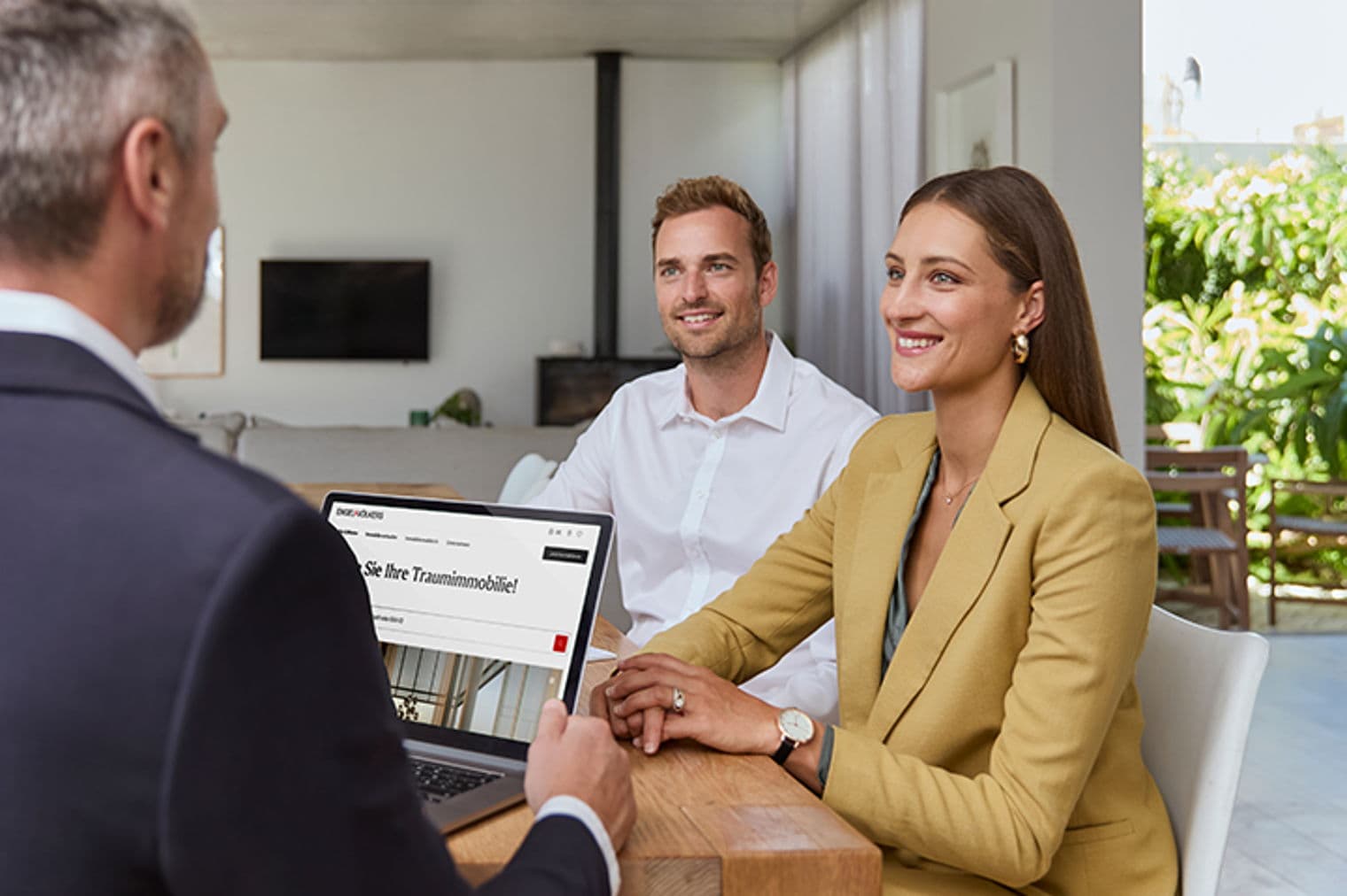 Ein Immobilienmakler zeigt einem Paar Immobilien auf einem Laptop. Das Paar lächelt.
