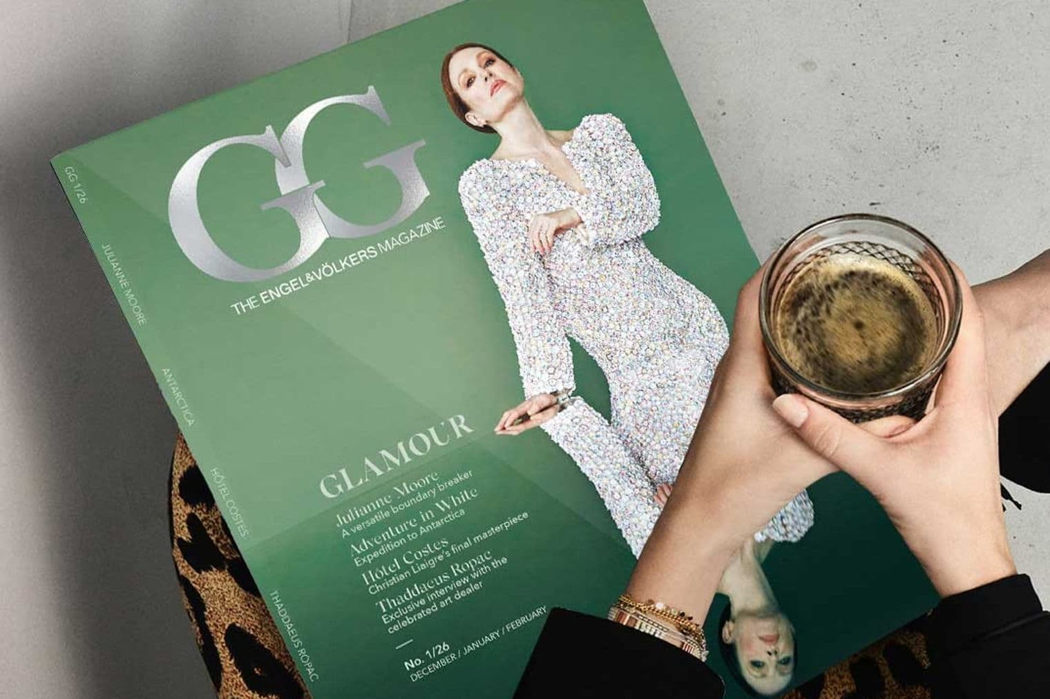 Nahaufnahme von Händen, die einen Kaffee über einer "GG"-Zeitschrift mit Julianne Moore auf dem Cover halten. Das Magazin ist grün und silberfarben.