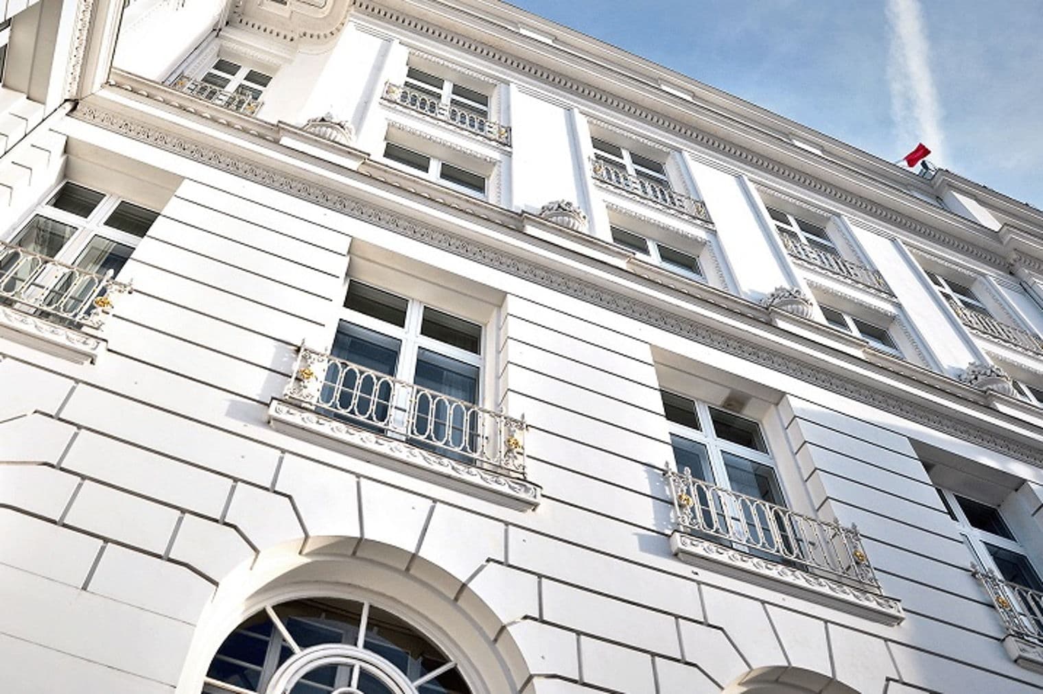 Niedrigwinkelaufnahme eines weißen Gebäudes mit Fenstern und dekorativen Balkonen vor einem blauen Himmel.