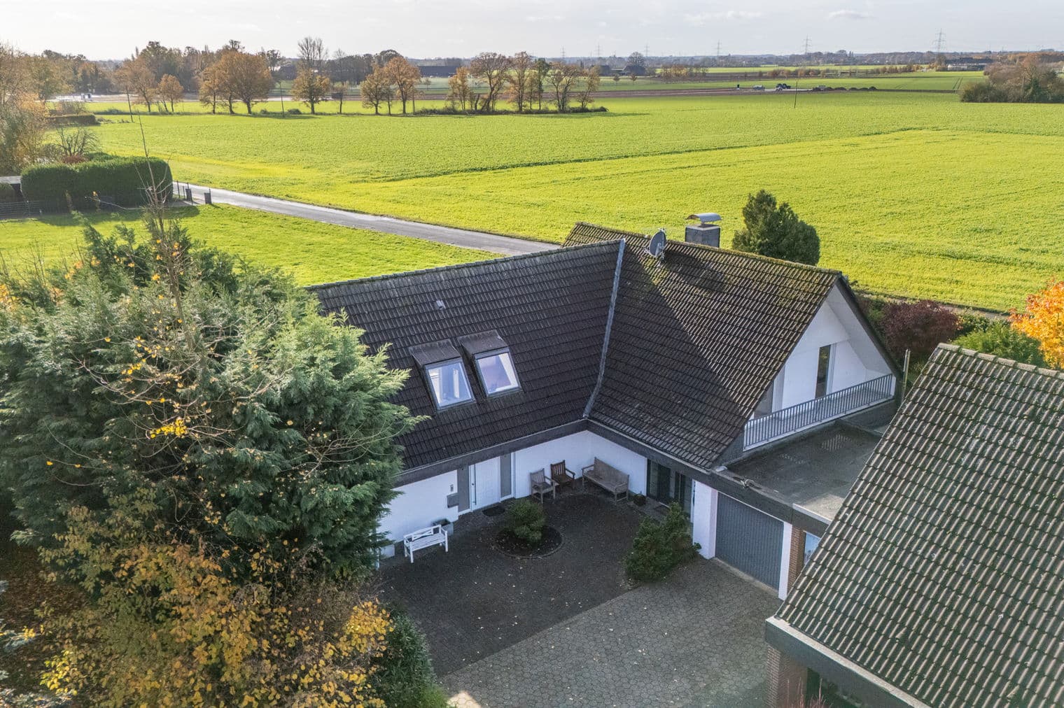 Aerial view of a white house with a dark roof, surrounded by green fields and trees.