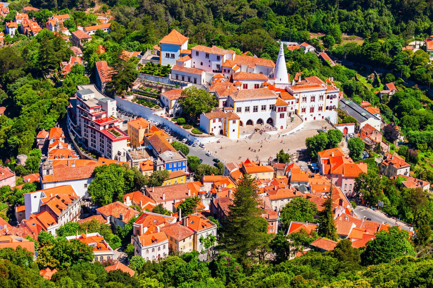 Aerial view of the Palace of Sintra, Portugal, with white walls, orange roofs, and surrounding green trees.