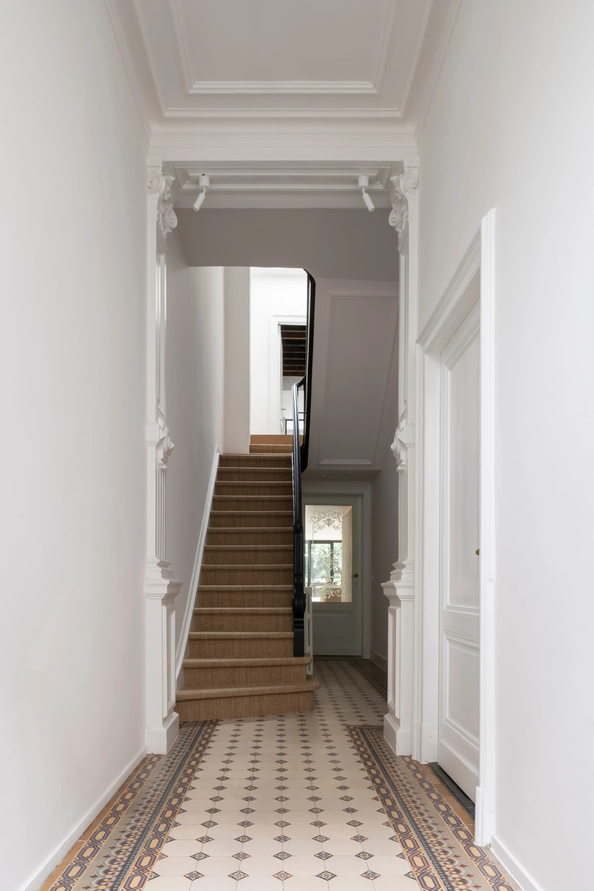 Hallway with white walls, patterned tile floor, and carpeted stairs. A door is open on the right.