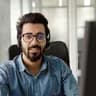 A man with glasses and a headset smiles in an office setting.
