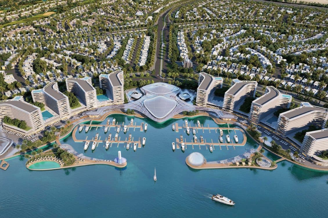 Aerial view of a modern beachfront resort with unique, curved buildings, numerous pools, two marinas, and a densely built residential area nearby.