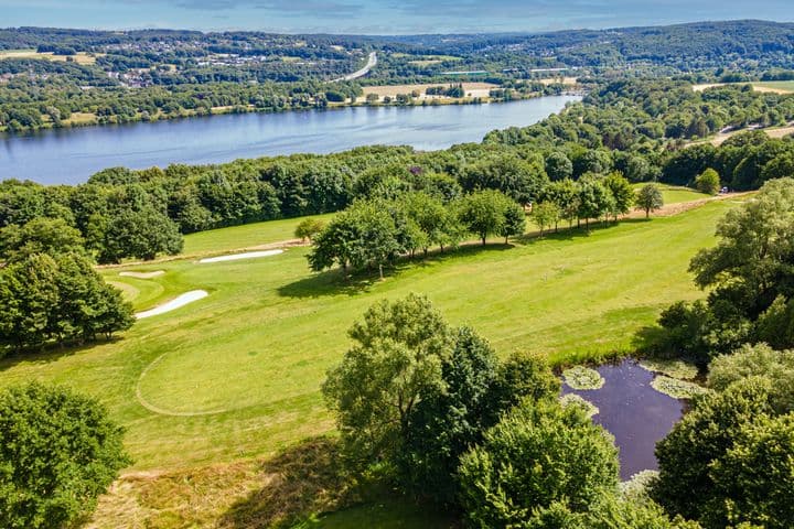 Aerial view of a green plot surrounded by trees, a pond, and a lake in the background