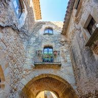 Vista de ángulo bajo de un callejón de piedra con una entrada arqueada y un balcón con plantas en macetas.