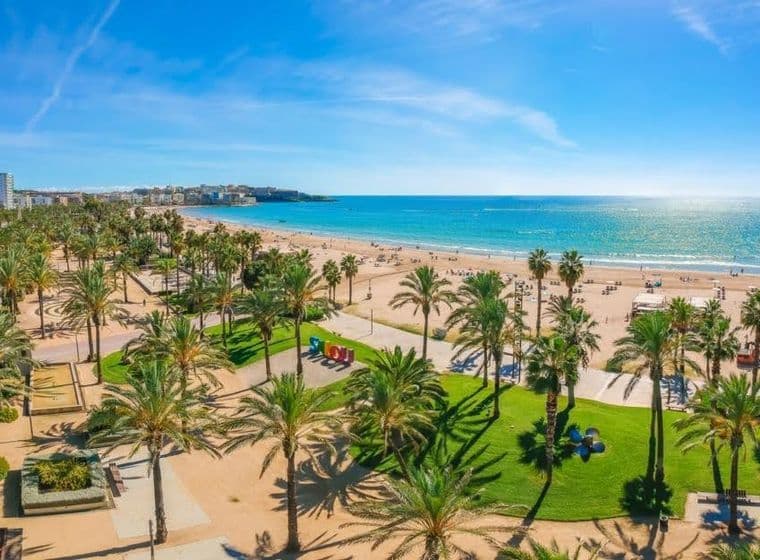 Playa de la Costa Dorada con palmeras, zonas verdes y edificios al fondo