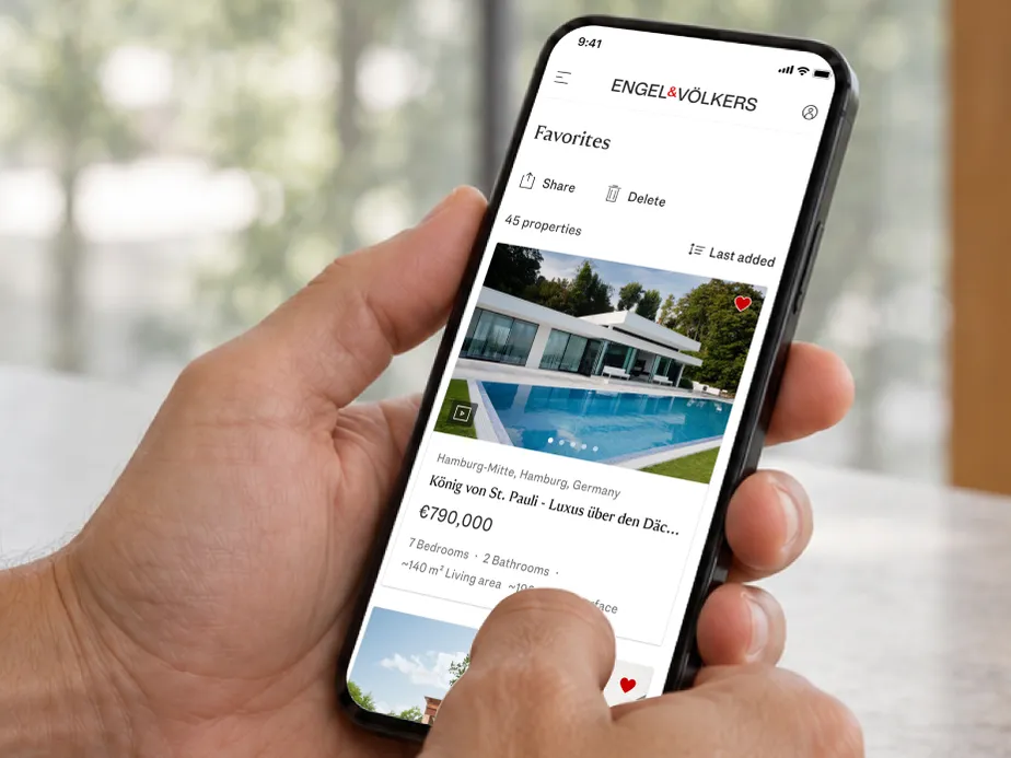 Hands hold a smartphone displaying a real estate website with a poolside modern villa listing in Hamburg, priced €790,000. AI-generated image