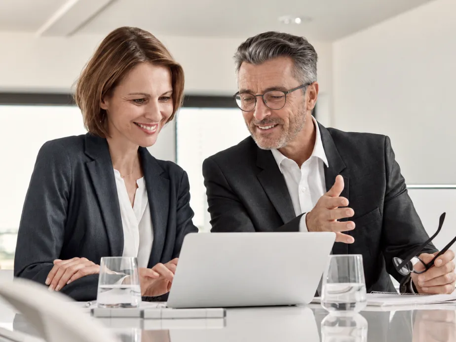 Customer and Agent in business attire sit at a conference table, smiling as they review a laptop together, with water glasses nearby. AI-generated image