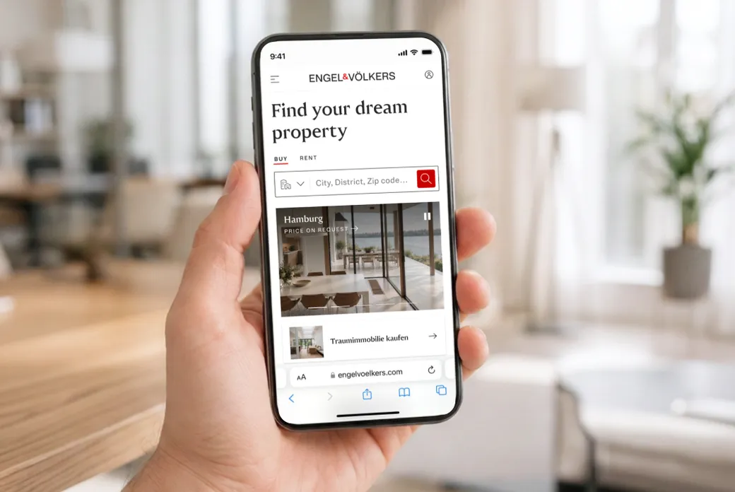 Hand holding a smartphone displaying Engel & Völkers real estate site with 'Find your dream property' search bar, bright living room backdrop. AI-generated image