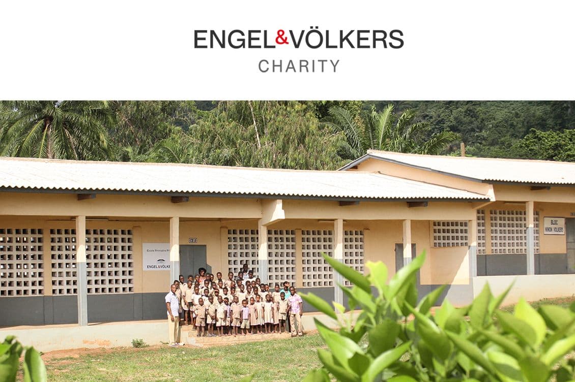 Engel & Völkers Charity: A group of children in uniforms stand in front of a school building with tropical trees in the background.