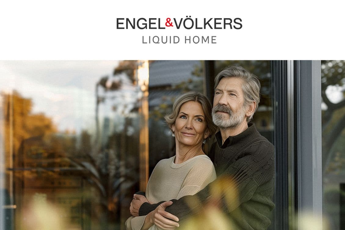 Mature couple standing by a glass window at sunset, with soft natural lighting. The couple is dressed casually, with the woman wearing a beige sweater and the man in a dark knit top, creating a warm and comfortable atmosphere beneath the Engel & Völkers Liquid Home logo.