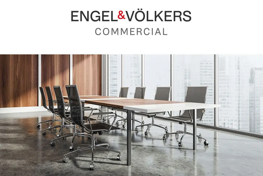 Engel & Völkers commercial office space with a long conference table and chairs. Large windows overlook a city skyline.