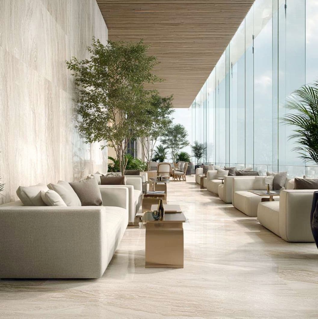 Spacious modern lounge with beige sofas, potted trees, and large glass windows offering a bright, airy atmosphere.