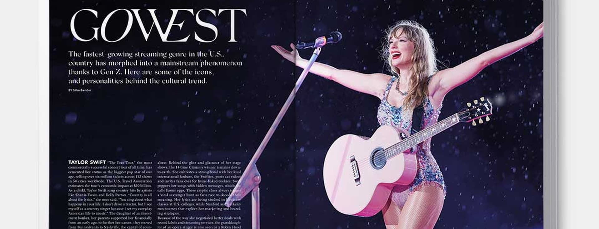 Taylor Swift on stage with a pink guitar, arms outstretched, wearing a sparkly blue outfit and silver boots.