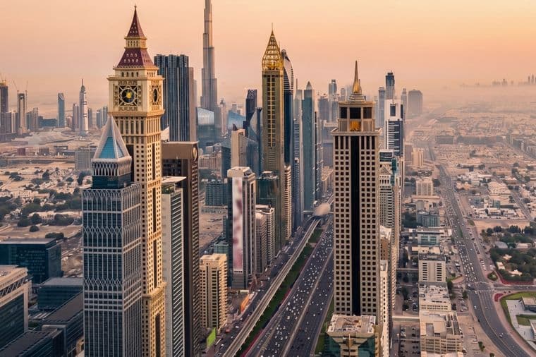 Aerial view of Dubai's skyline at sunset, featuring iconic skyscrapers and busy streets under a warm, hazy sky.