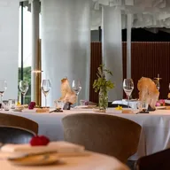 Elegant dining table set with wine glasses, plates, and a glass vase of greenery; rock-like centerpieces and a modern interior with white columns.