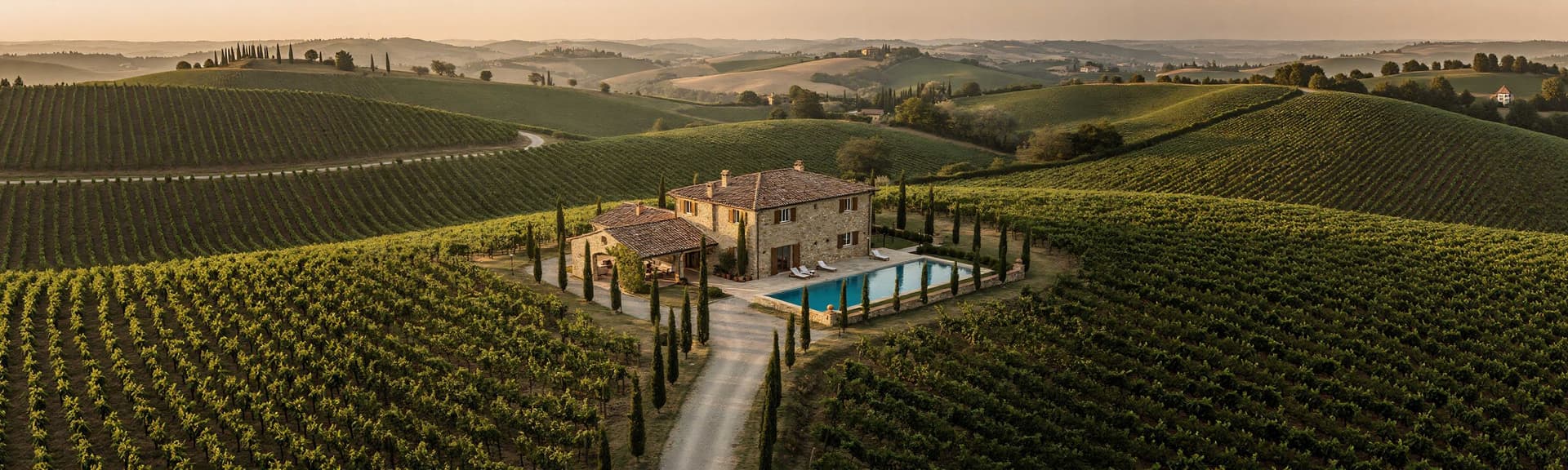 Aerial view of a villa with a pool surrounded by lush vineyards and rolling hills at sunset.