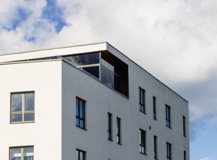 Modern wit gebouw met donkeromlijste ramen tegen een blauwe lucht met witte wolken.