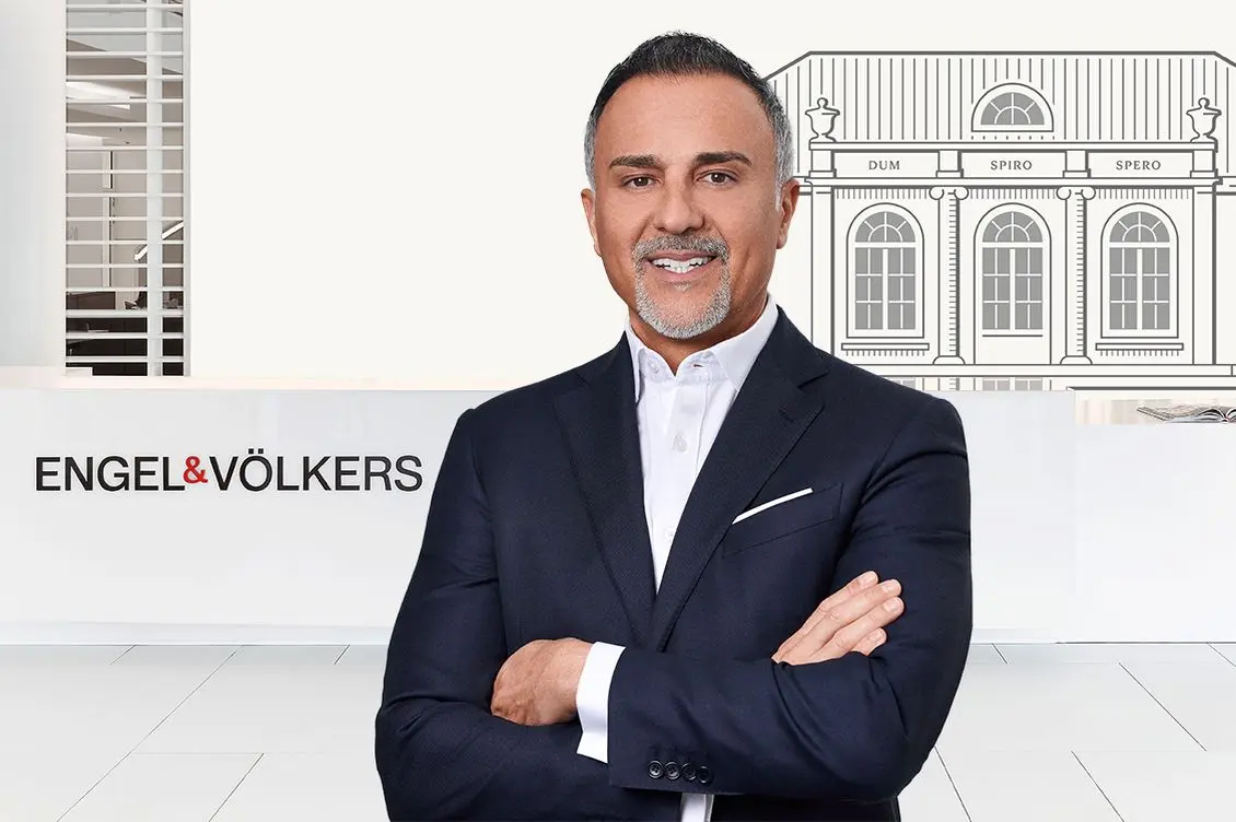 Engel & Völkers CEO Jawed Barna stands in front of the reception. In the background, the logo and the iconic villa are visible.