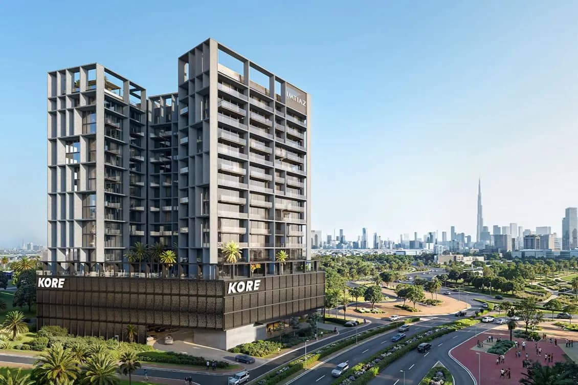 Modern concrete twin-tower complex on a dark podium labeled KORE; palm trees, curved roads, and a distant city skyline.