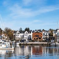 Der sonnige Hafen von Laboe mit Segelbooten und Yachten, die vor bunten Häusern am Wasser vor Anker liegen, blauer Himmel und Spiegelungen auf dem ruhigen Wasser