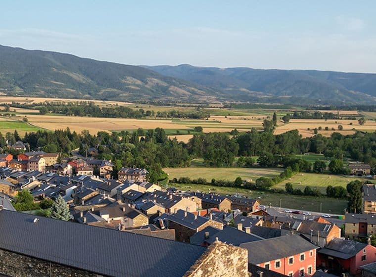Església de Llívia en primer pla, seguida de cases, camps i muntanyes.