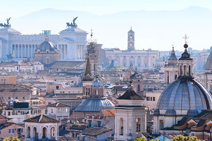 Panoramic view of Rome's skyline showcasing iconic landmarks such as the Altare della Patria (Victor Emmanuel II Monument) and church domes. The dense historical cityscape reflects the high property prices in Rome, with ancient and modern buildings coexisting in this sought-after real estate market.
