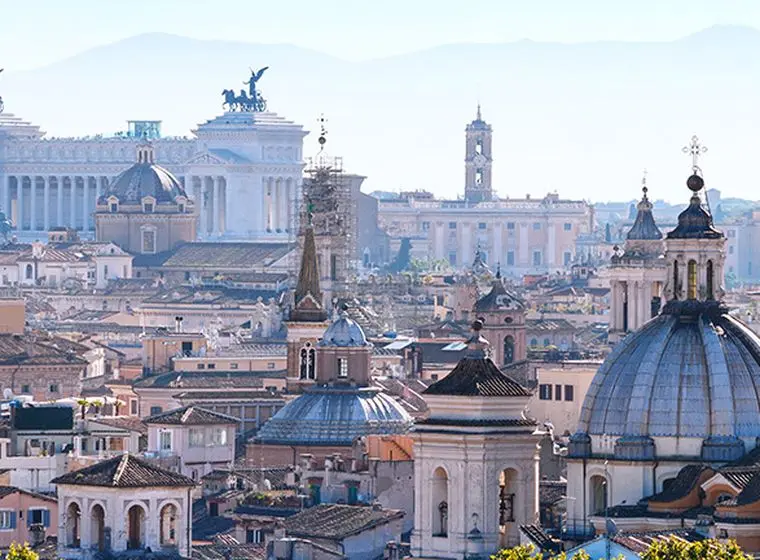 Panoramic view of Rome's skyline showcasing iconic landmarks such as the Altare della Patria (Victor Emmanuel II Monument) and church domes. The dense historical cityscape reflects the high property prices in Rome, with ancient and modern buildings coexisting in this sought-after real estate market.