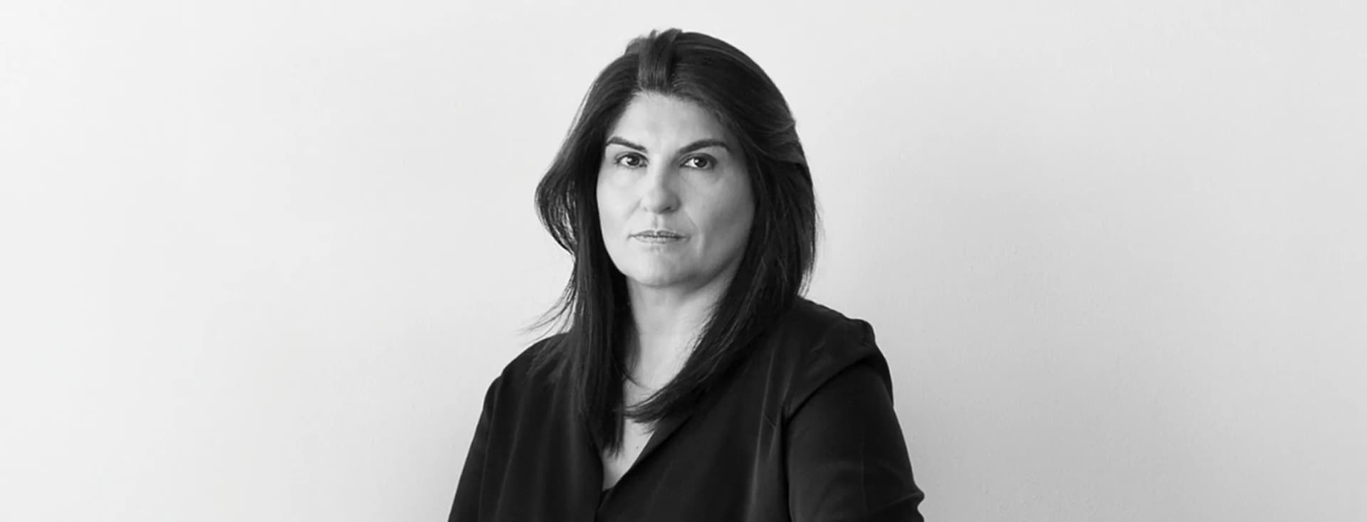 lack and white portrait of a woman with dark shoulder-length hair looking directly at the camera against a minimalist studio background.