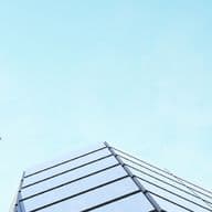 Looking up at modern glass skyscrapers against a clear blue sky, reflecting the light and creating dynamic geometric patterns.